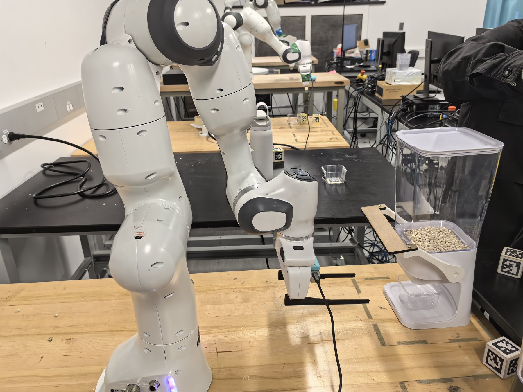 Close-up of a Franka Panda arm operating a cereal dispenser with AprilTags nearby